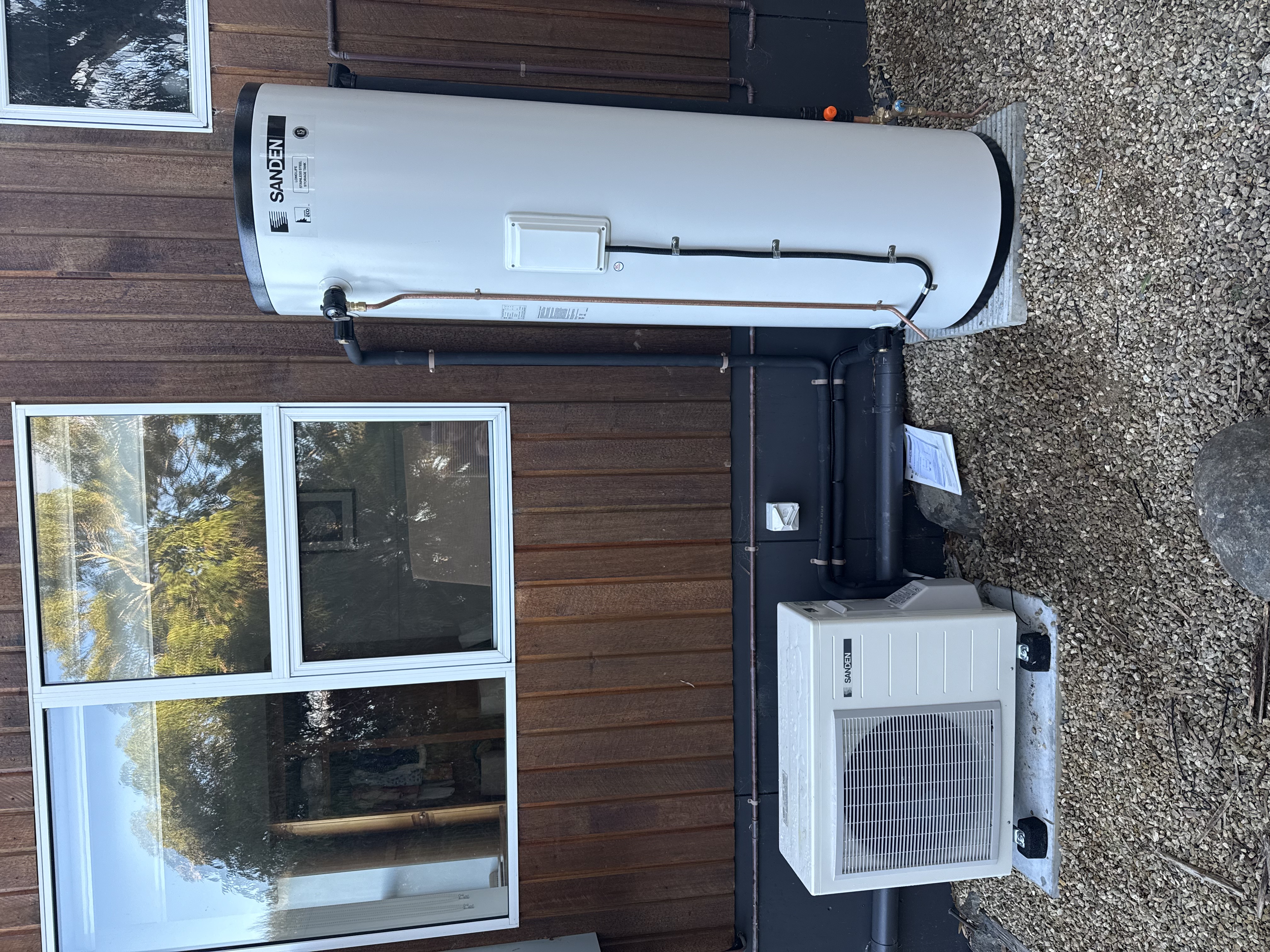 Sanden heat pump hot water system installed on exterior of timber home